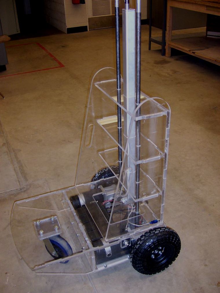 The Nomad assembled: a transparent acrylic camera cart on rubber wheels with a vertical mast for the camera head, on a workshop floor.