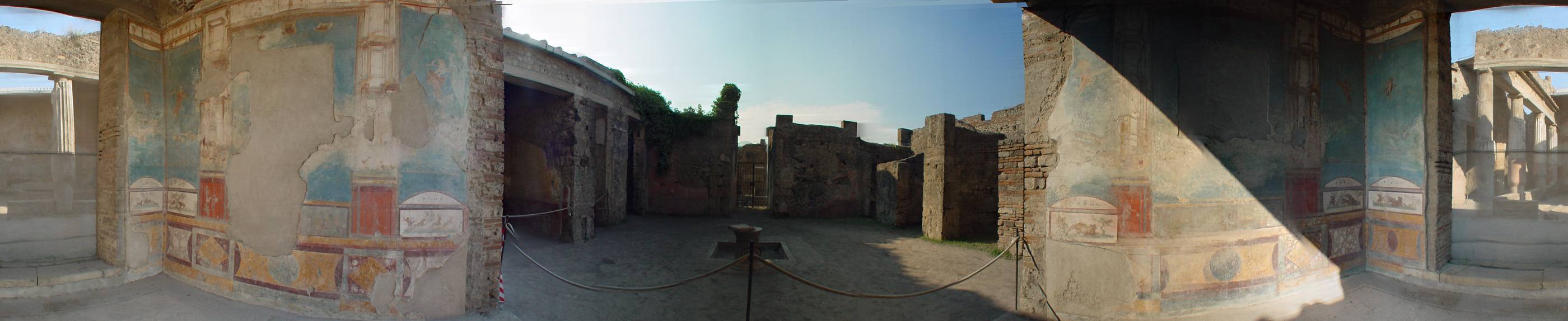 A 360° panorama of the House of the Ancient Hunt at Pompeii: frescoed walls in blue and ochre around an open, roped-off courtyard under a low afternoon sun.